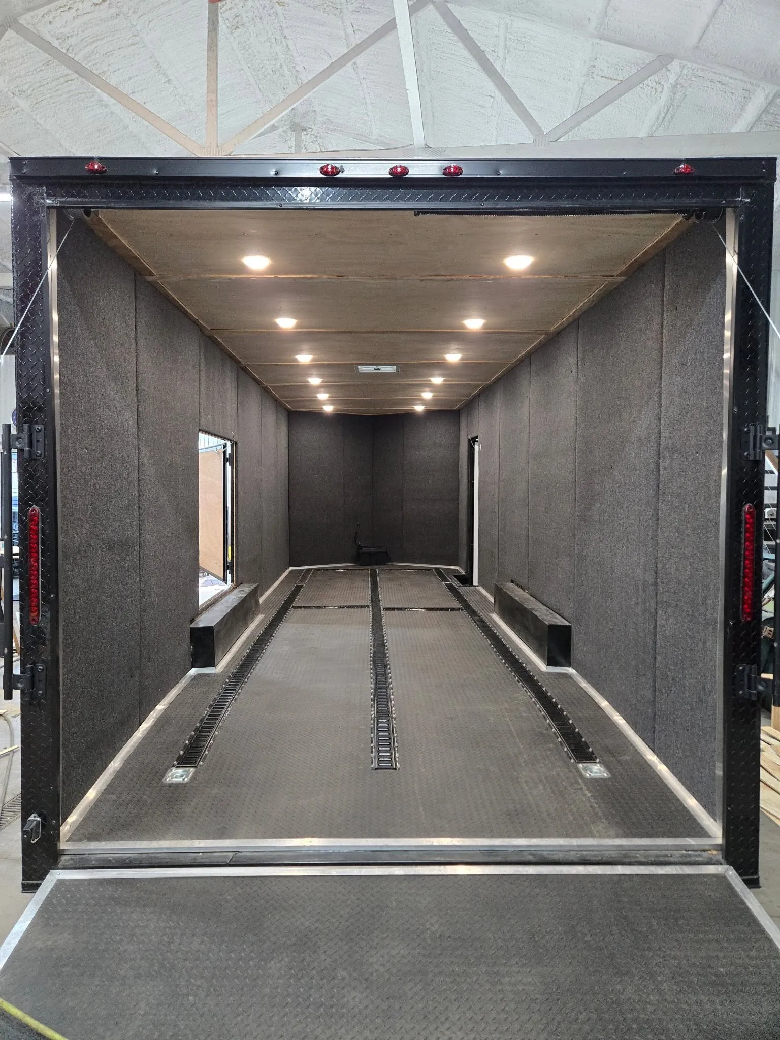 Carpeted car hauler interior with recessed floor tie-down track and ceiling lights.